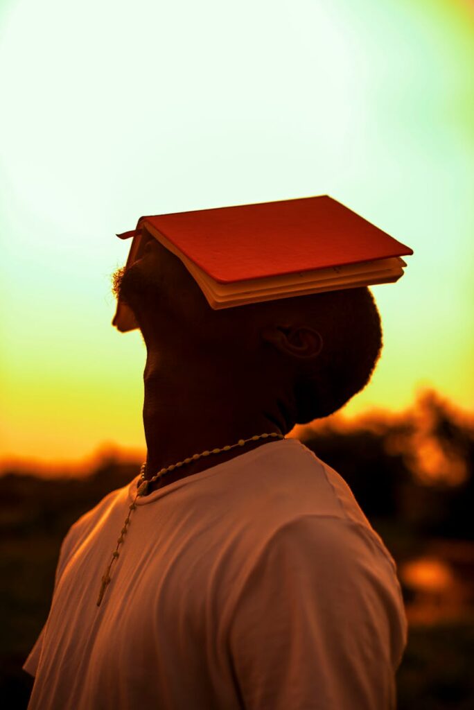 Young man balancing a book on his head at sunset outdoors.