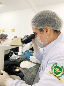 Scientist in lab gear examining samples under a microscope in genetics lab