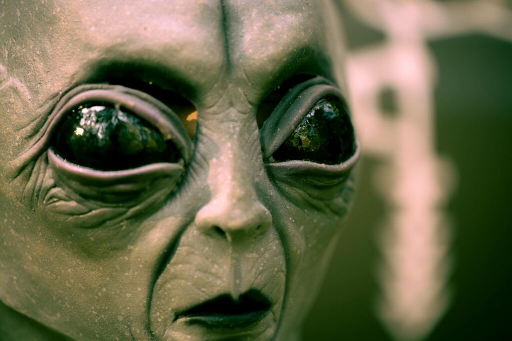 Close-up of alien face with large black eyes in dark, shadowy setting