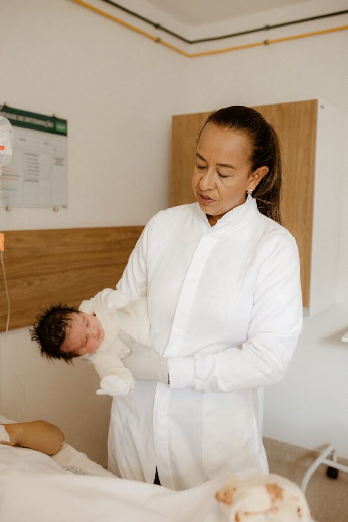 Healthcare professional in white coat holding newborn in hospital room.