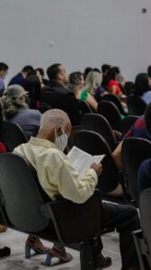 Elderly man wearing a mask reading a book at a crowded indoor event. (Incomplete: max_output_tokens)