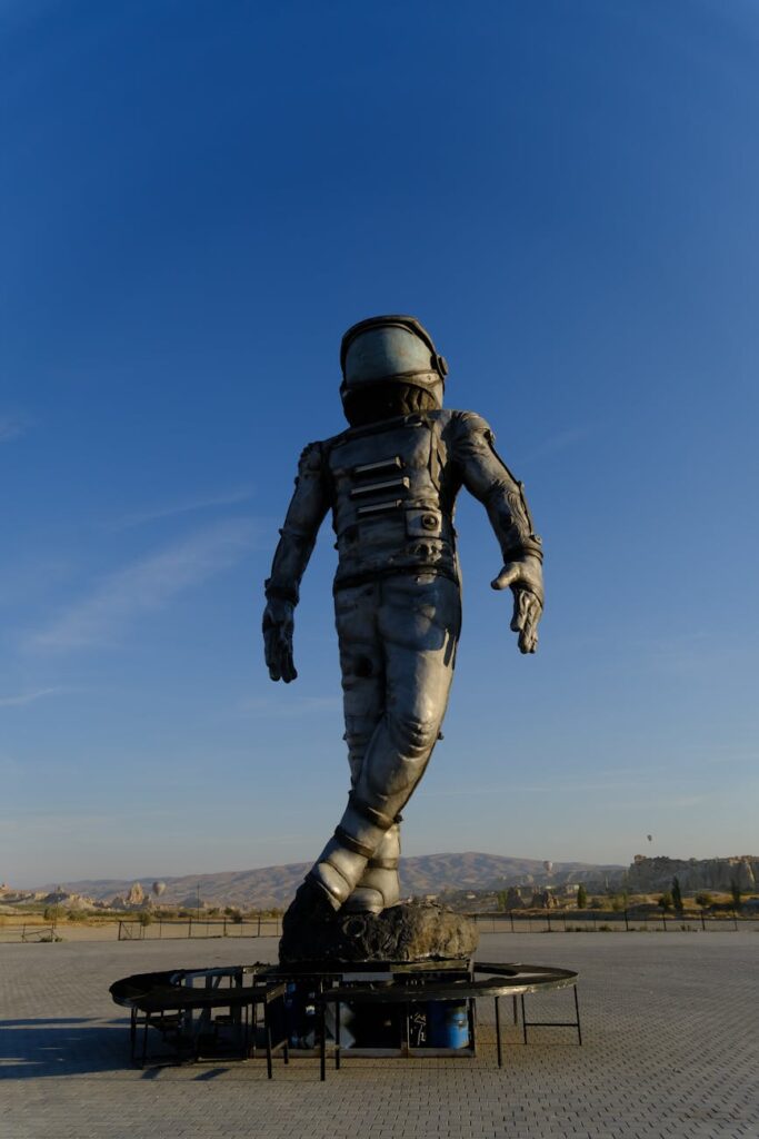 Giant astronaut sculpture in open desert under clear blue sky.