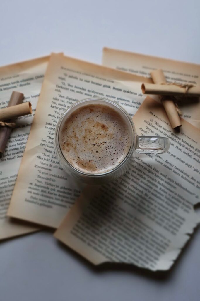 Cup of coffee on open vintage book pages with cinnamon sticks