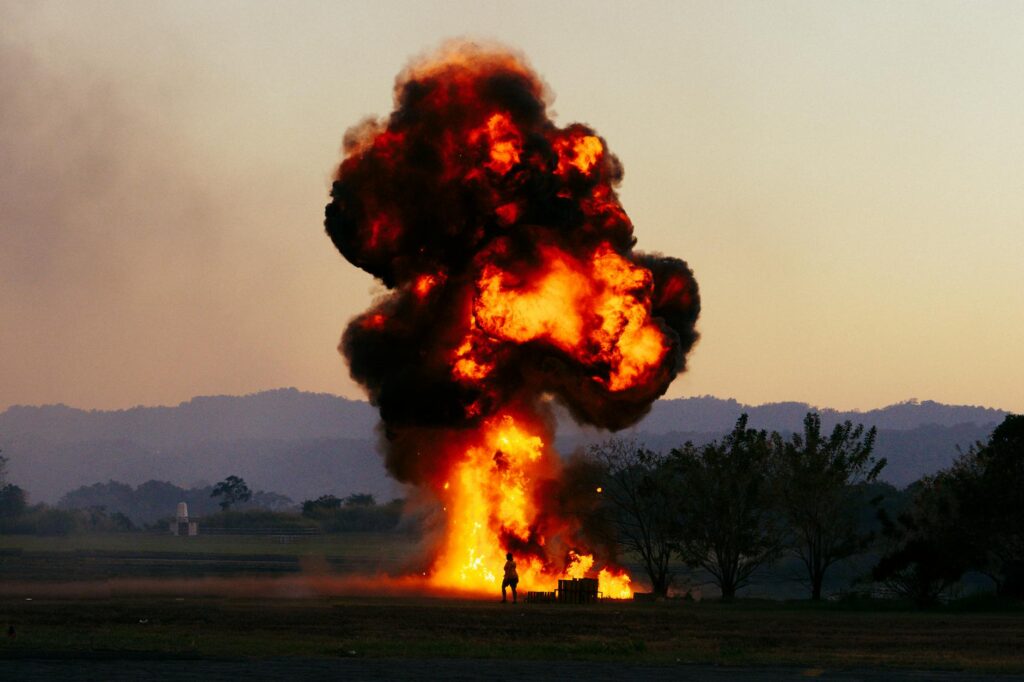 Massive fiery explosion with thick smoke rising over an open field