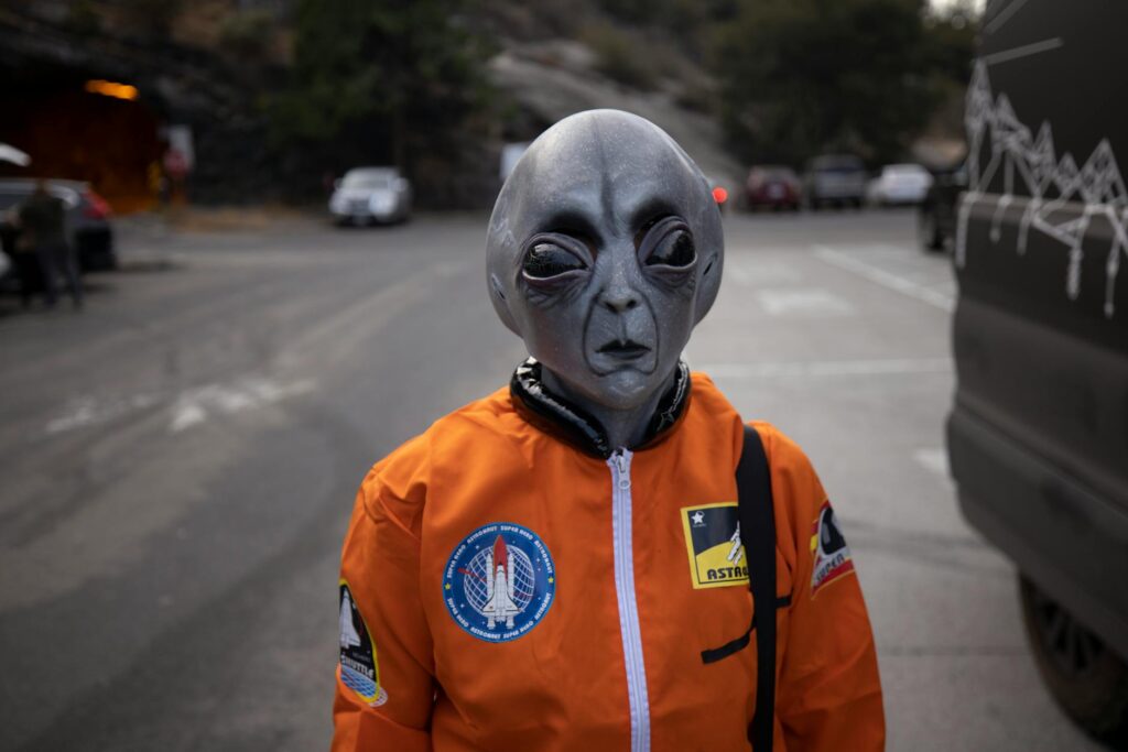 Person in alien mask and orange astronaut suit standing on a city street