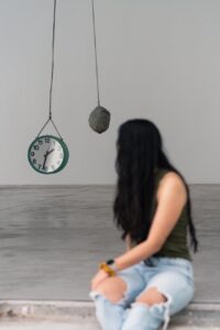 Woman sitting on concrete steps with hanging clock and rock behind her
