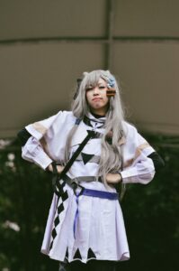 Cosplayer with long silver hair in white and black anime-style costume indoors
