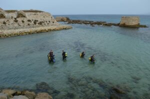 Scuba divers exploring clear coastal waters near rocky shore at (Incomplete: max_output_tokens)