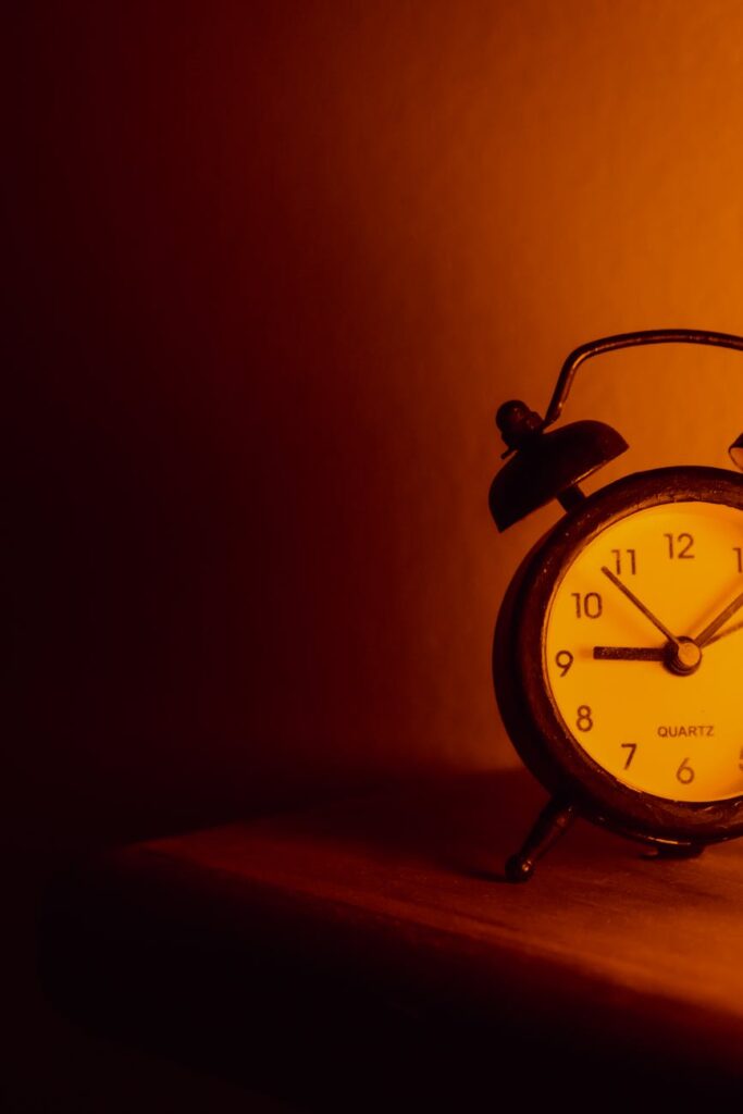 Vintage alarm clock glowing in warm orange light on a wooden table.