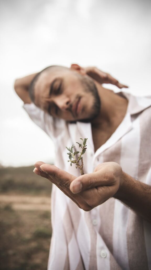 Young man holding a small plant outdoors with blurred background.